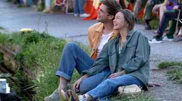 a white man and women sit on a patch of grass smiling
