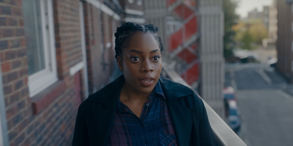 A black woman stands on a London housing estate balcony