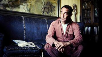Derek Jarman looks at the camera while sitting on a sofa