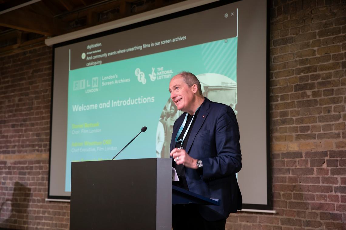 Adrian Wootton speaking at lectern with 'Welcome' slide in background