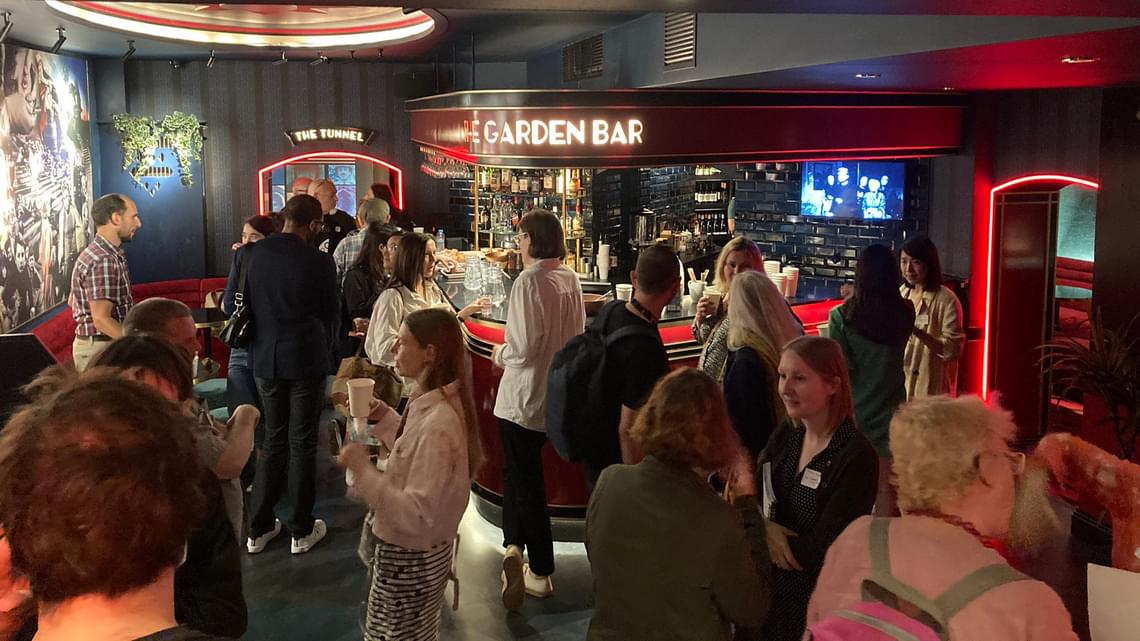 A crowded bar with film-related murals on the wall, and a neon 'Garden Bar' sign