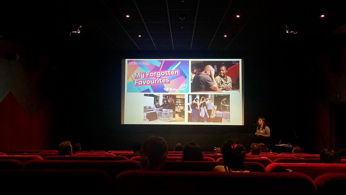Storyhouse Cinema Assistant Isobel Harrop addresses an audience in a cinema, in from of a screen with slides of people in cinemas, and the headline 'My Forgotten Favourites'