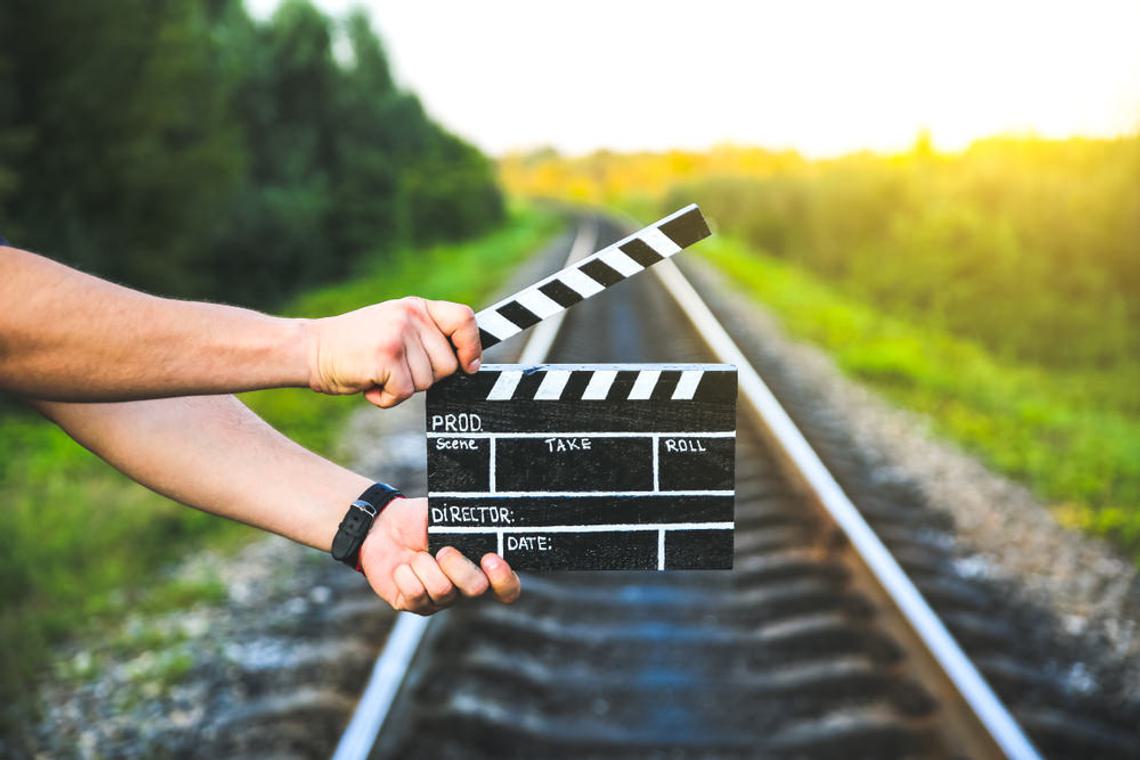hands holding clapperboard in front of railway track and field