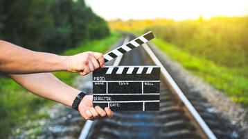hands holding clapperboard in front of railway track and field