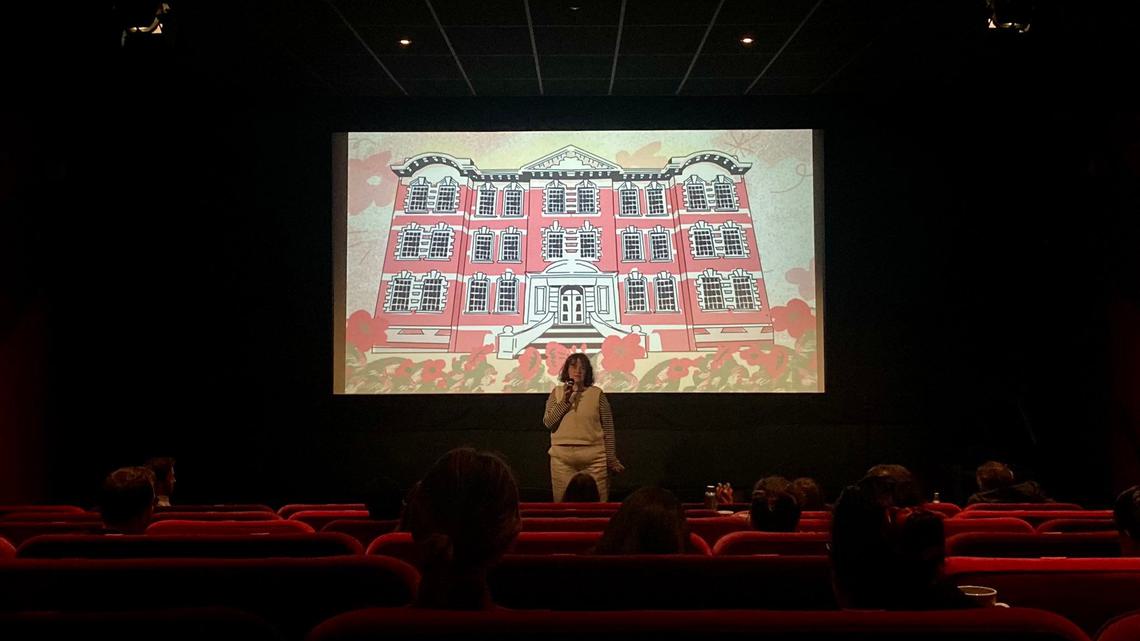 FAN Young Consultant Thea Berry addresses an audience in a cinema, in front of a screen with an illustration of a large building